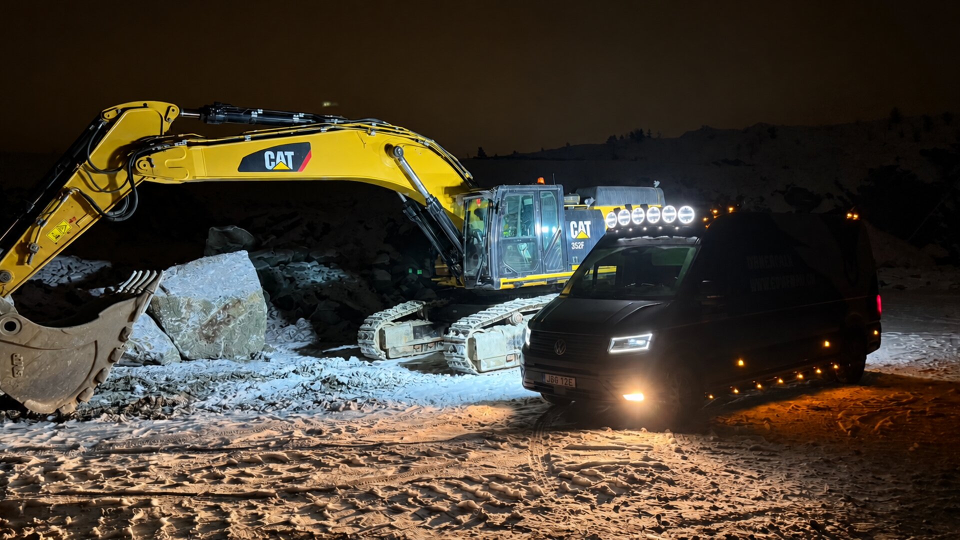 CAT-grävmaskin och Unnerfalk servicebil på arbetsplats nattetid
